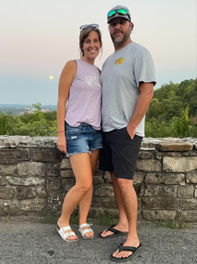 Matt and his wife in front of a low stone ledge with the sun low in the sky.