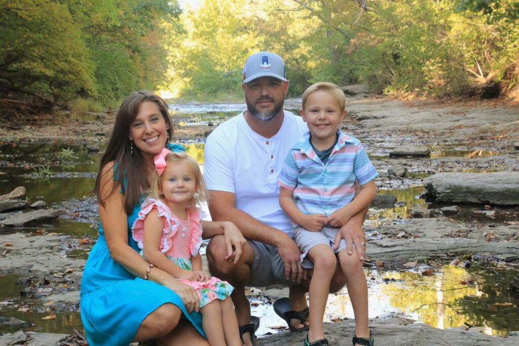 Matt with his wife, son, and daughter on a rocky area with standing water surrounded by lots of trees.