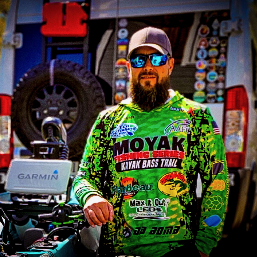 A man in sunglasses with a bright green shirt covered in sponsor logos.
